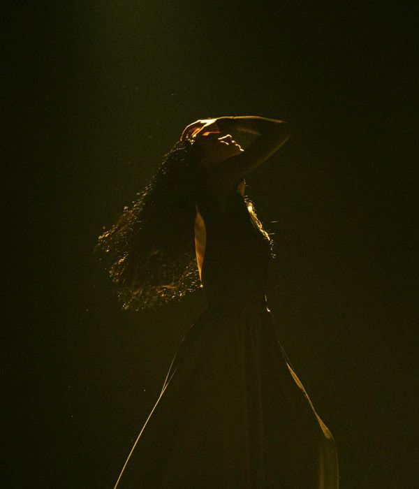 Woman in a dynamic yet graceful movement pose against a dark background with violet light.